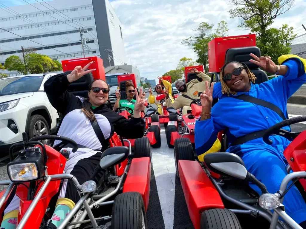 IMG_4143 - StreetKart Group of friends riding red pedal go-karts on a city street, smiling and flashing peace signs at the camera.